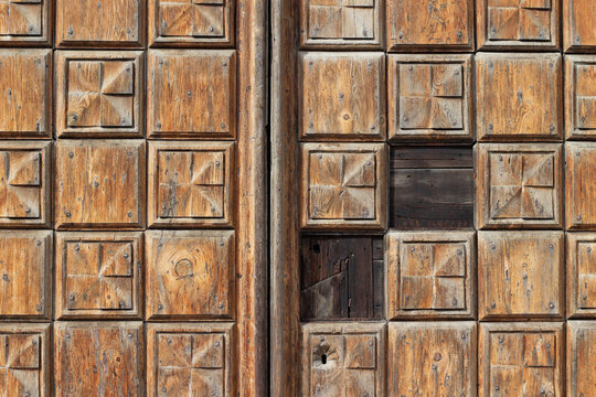 Detailed wooden door with geometric patterns and textures, featuring a small opening and weathered surface, showcasing craftsmanship and natural aging effects