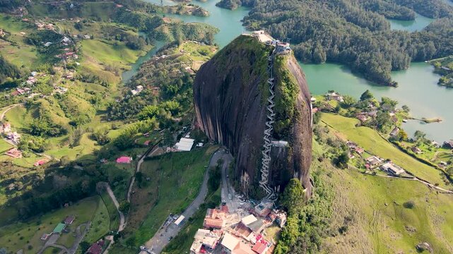 A stunning aerial shot captures the iconic El Pe&ntilde;ol rock with lush green hills and the shimmering lake below in Guatap&eacute;, Colombia.