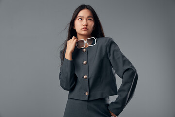 Young Asian woman posing in stylish dark gray outfit holding white sunglasses looking away in...