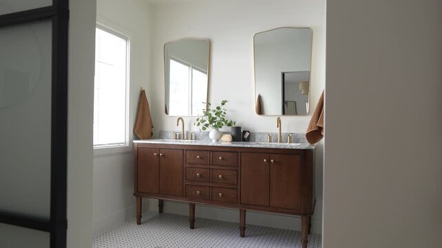 Slow push-in shot of a luxury bathroom interior featuring a wooden double vanity, marble countertop, gold fixtures, modern mirrors, and natural window light. Elegant contemporary home remodel