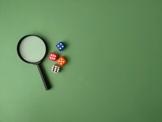 A high-angle, conceptual still life featuring a black magnifying glass and four colorful dice on a...