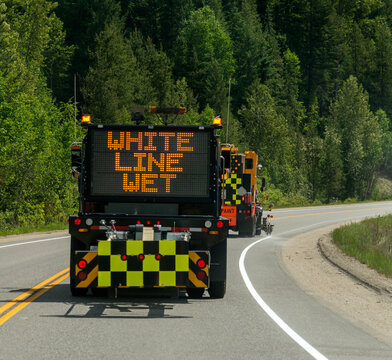 Canada, BC, Valemount.  Road crew painting line on the side of highway 5 in mountainous terrain.