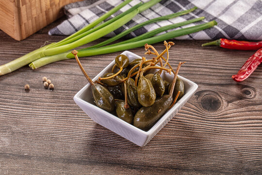 Pickled caper berries in a bowl with fresh ingredients on a rustic wooden table.