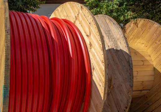 Large industrial wooden cable spools with red empty conduits for fiber optic installation on a construction site