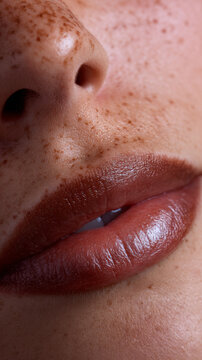 Close up of lips with brown lipstick and freckled skin showing natural texture and pores