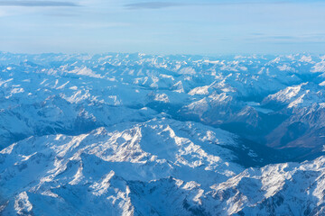 Fototapeta premium Plane view of mountains at sunrise, snow rock and blue cloudy sky aerial view