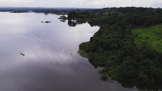 Fast forward motion airborne view of lake, with an unrecognizable fisherman, and its surronding landscape with forest amd mountains in the background during overcast weather.