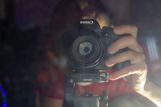 A young man holding a professional camera and filming in a dark nightclub with colorful lights