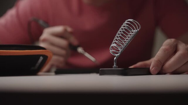 Technician hand placing soldering iron into spring stand for electronics repair and maintenance, focusing on technical work, precision and hand skills, close-up cropped shot. Shooting in slow motion.
