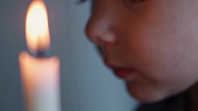 Child Gazes Softly. Gentle Child Watches Glowing Candle Flame. Young Girl Or Boy Fixates On Gentle Candle Glow Indoors. Young Child Stares Quietly At Luminous Candle In Calm Indoor Surroundings