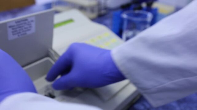 A scientist uses a spectrophotometer to determine substances in a cuvette, places the cuvette in the device and presses buttons.