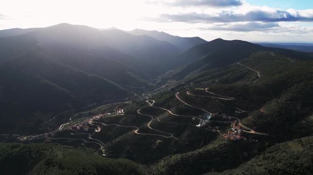 Drone shot of small village nestled in green mountain valley with winding roads and forest in Extremadura Spain. Scenic rural landscape and European travel destination.