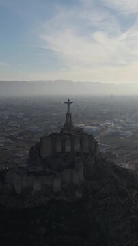 Drone flying toward the scenic silhouette of Christ of Monteagudo statue on a hilltop with fog in the horizon. Vertical.