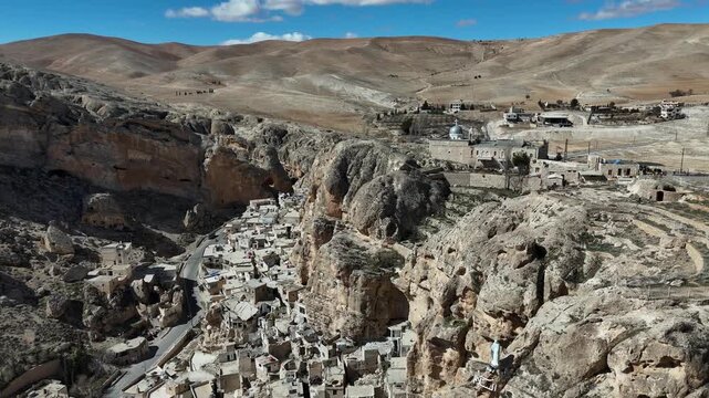Drone view of the rugged mountain landscape in Ma'loula, Syria, featuring buildings and solar panels on top of sheer limestone cliffs