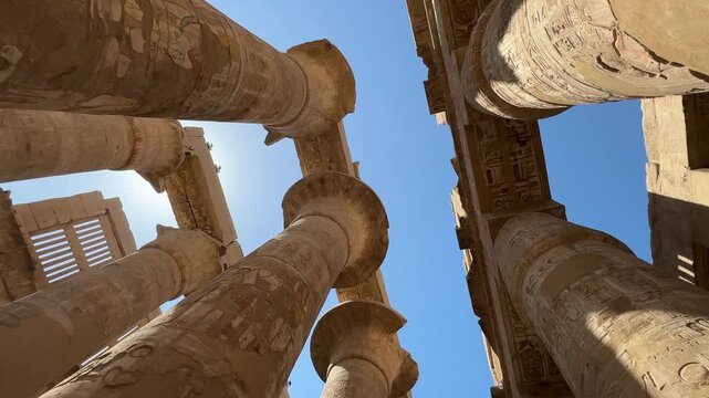 A cinematic low angle shot looking up at the massive stone columns with papyrus capitals and ancient hieroglyphs in the Great Hypostyle Hall of Karnak Temple