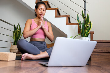 Asian woman meditating at home using online yoga class