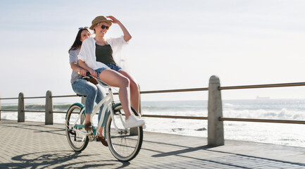 Happy, cycling and friends on bicycle by ocean for travel on weekend, summer holiday and vacation. Outdoor, promenade and women on bike for sightseeing, hobby and bonding for tourism or adventure © peopleimages.com