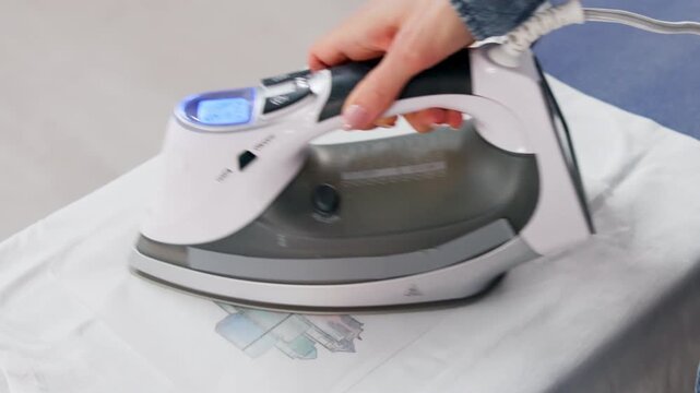 Woman Using Iron-On Heat Transfer To Apply Custom Design On T-Shirt