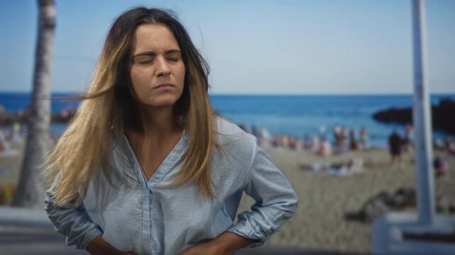 Woman holding hand on stomach while clutching shirt hem on a street beside a beach promenade; discomfort solitude reflection.
