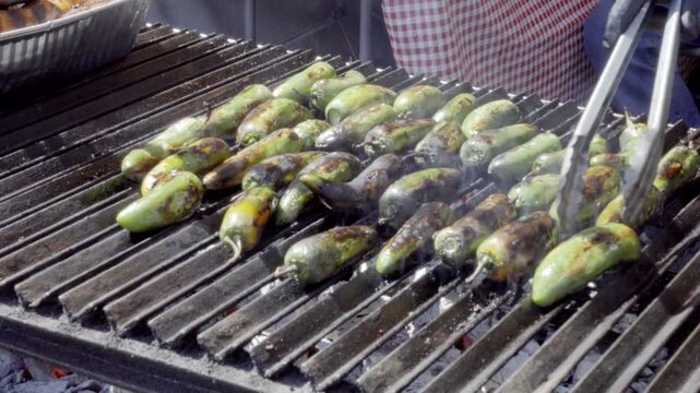 Close up of green peppers roasting on a grill at a street food stand during a lively festival in Cholula Puebla Mexico.