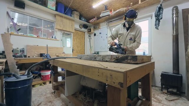 Craftsman in PPE Planing Timber Slab in Sunlit Garage Workshop Static Wide Angle
