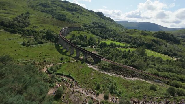 Cinematic FPV shot follows the iconic steam locomotive as it chugs across the Glenfinnan Viaduct. The train&mdash;real-life inspiration for the famous wizarding school express&mdash;glides past Loch Shiel