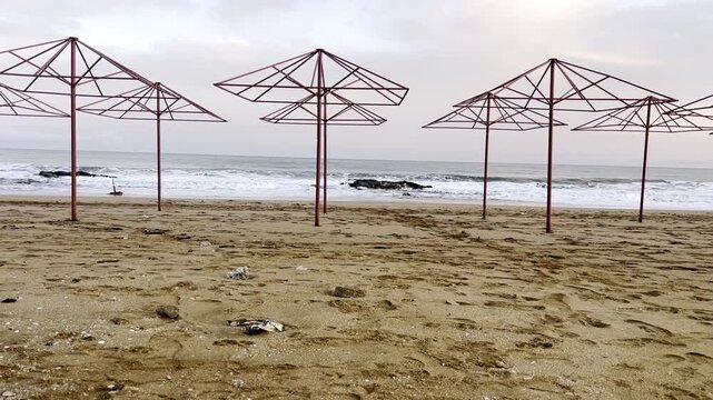 Some metal umbrellas stand on the beach as waves crash against the sand during early morning.