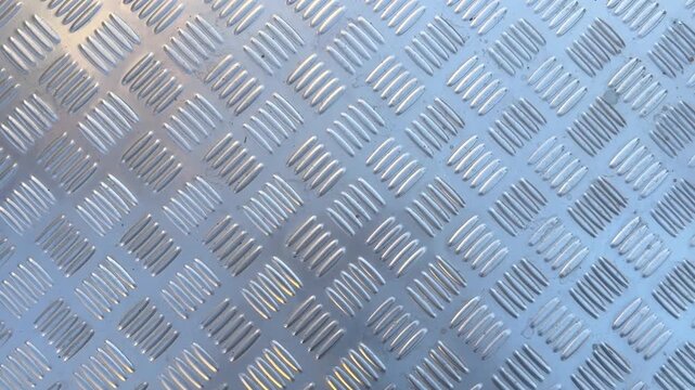 Video of silver metal checker plate surface with raised diamond tread pattern forming industrial textured background