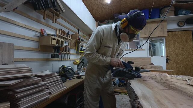Woodworker in PPE Pushing Electric Planer Across Massive Timber Slab Side Tracking Shot
