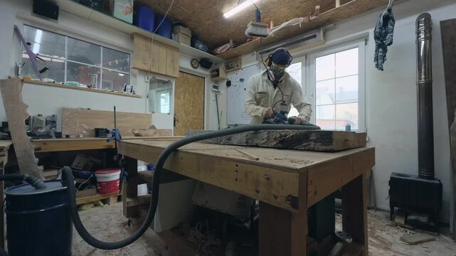 Woodworker in PPE Surfacing Slab near Wood Stove and Dust Collection Barrel Wide Angle Shot