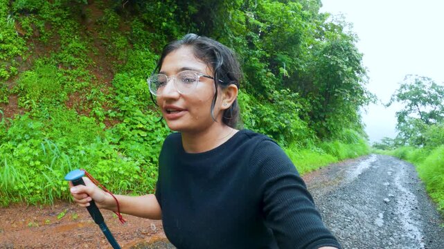 4K video of Indian teenager girl vlogging during hiking in Sahyadri Hills in Maharashtra, India. Hiker female holding hiking stick. Travel influencer vlogging during heavy rain in monsoon 