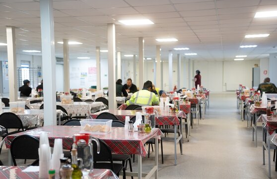 Industrial engineers sitting in canteen and talking on lunch break. Construction company workers in safety uniform eating meal and chatting in modern office