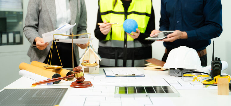 Legal and engineering professionals reviewing building plans with justice scale, gavel and safety equipment, symbolizing construction law, property regulation