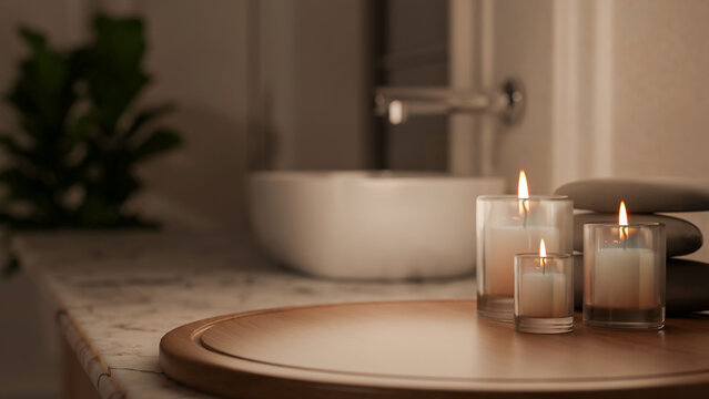 Glass candle and spa stone on wooden tray at marble sink counter in dim lit bathroom of modern house