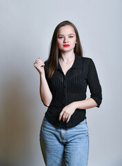 Naklejka premium Junge Frau in Jeans und schwarzer Bluse posiert selbstbewusst vor hellem Hintergrund. Modernes Fashion- und Lifestyleporträt mit Copyspace, Konzept für Stil, Mode und Persönlichkeit.