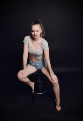 Naklejka premium Selbstbewusstes Model sitzt auf einem Hocker im Studio und blickt direkt in die Kamera. Modernes Fashion-Porträt mit natürlichem Stil, Konzept für Mode, Lifestyle und Persönlichkeit.