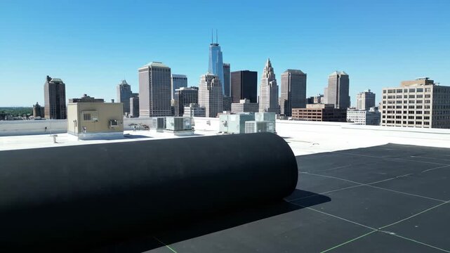 Commercial flat roof installation with a large black waterproofing membrane being unrolled. Rooftop construction and building maintenance in a modern downtown city