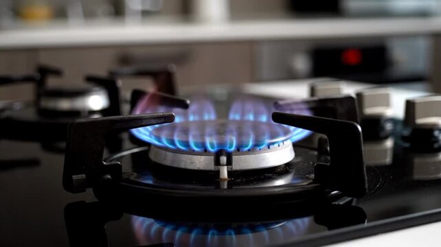 Close up of a gas stove burner igniting with a bright blue flame. Sequence showing the ignition process on a modern kitchen hob for cooking and domestic heating concepts