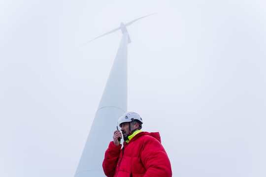 Technician with helmet inspects wind turbine outdoors in fog