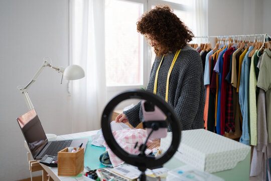 Fashion designer packaging garment at home office workspace with video setup