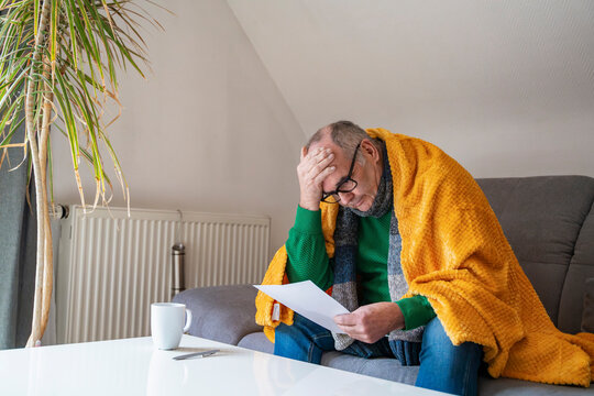 Worried person with blanket and bill on sofa during cold season