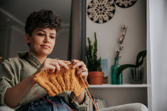 Woman knitting with warm wool yarn at home in cozy living room