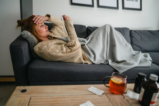 Person with flu and fever resting on couch with medicine and hot tea