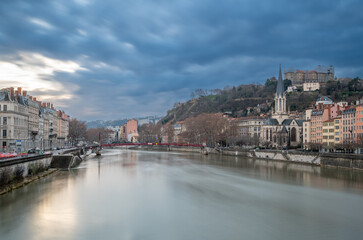 Fototapeta premium Lyon, france. December 29, 2023. Lyon cityscape showing the saône river, saint-georges church, and historic buildings under a cloudy sky during blue hour