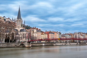 Fototapeta premium Lyon, france. December 29, 2023. Lyon cityscape along the saône river, featuring saint-georges church spire and the red passerelle saint-georges bridge