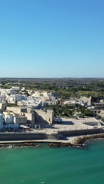 Aerial view of the Otranto coastline featuring turquoise sea, historic architecture, and a bright, clear sky. The scene captures the charm of this Italian coastal town.