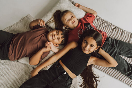 Happy siblings lying together enjoying time at home on mattress