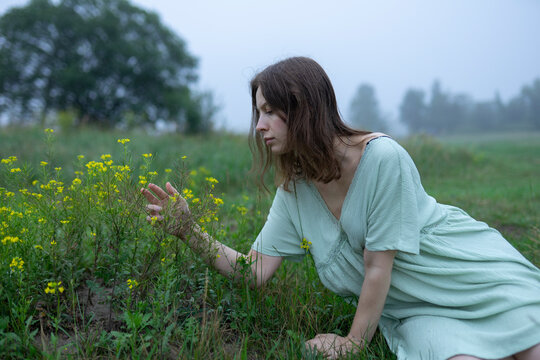 Woman in dress kneeling in foggy morning meadow with yellow wildflowers