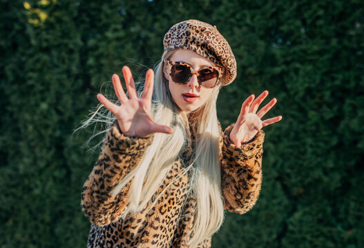 Stylish person in leopard jacket and beret posing outdoors in garden