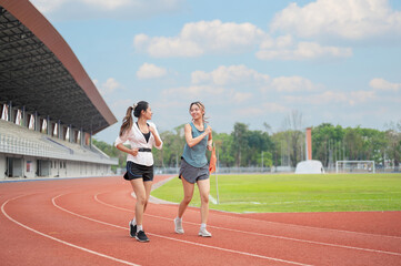 Obraz premium Athletic asian women friend talking as running jogging on racetrack in sports stadium under blue sky